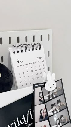 a desk with a calendar, photos and an alarm clock on the wall next to it