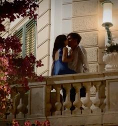 two people standing on a balcony kissing each other