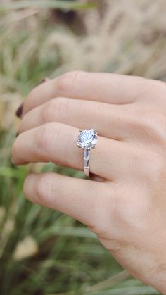 a woman's hand with a diamond ring on her finger, and grass in the background