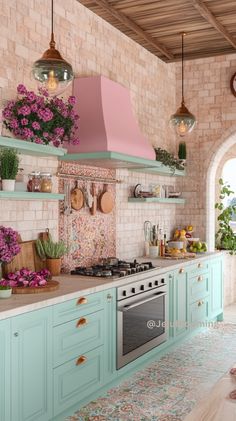 a kitchen with green cabinets and pink flowers on the counter top, along with potted plants