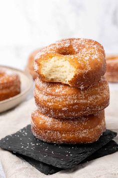 a stack of doughnuts sitting on top of a black slate board with powdered sugar