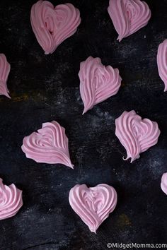 pink frosted heart shaped cookies sitting on top of a black counter next to each other