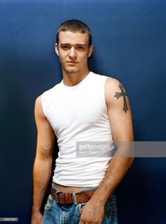 a young man posing for the camera in front of a blue wall wearing jeans and a white tank top