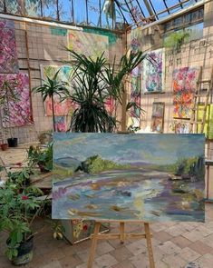 an artist's easel with paintings on the wall and plants in pots next to it