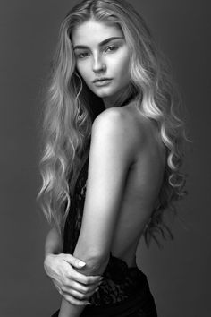 a woman with long blonde hair is posing for a black and white photo, she has her back turned to the camera