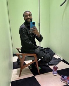 a man sitting on a chair taking a selfie with his cell phone in the bathroom