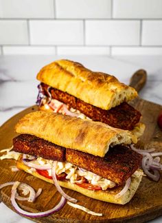 two sandwiches are on a cutting board with onions