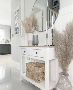 a white table with a mirror, vase and some dried grass in it on the floor