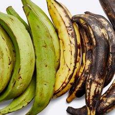 several different types of bananas lined up in a row on a white surface with brown spots