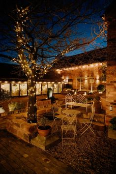 the patio is lit up at night with fairy lights strung from the trees and chairs