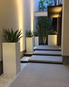 some white planters are on the side of a building with plants in them and gravel