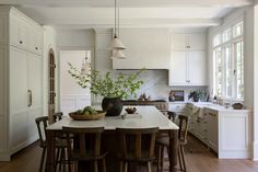 a large kitchen with white cabinets and wooden flooring, along with a dining table surrounded by bar stools