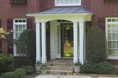 the front entrance to a large brick house with white trim and columns on either side