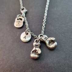 two silver necklaces with charms on them sitting on a black surface, one has a pair of boxing gloves and the other has a key