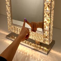 a person is pointing at their reflection in a mirror that's lit up with lights