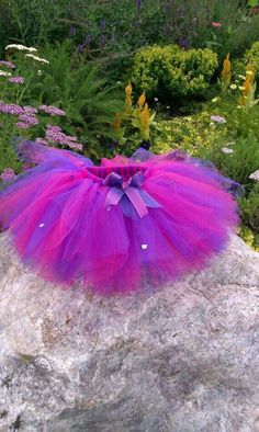 a purple and pink tutule sitting on top of a rock in front of flowers