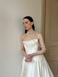 a woman in a white wedding dress leaning against a wall with her hands on her hips