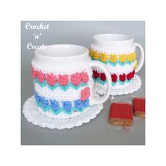 two coffee mugs with crochet on them next to some cookies and candy