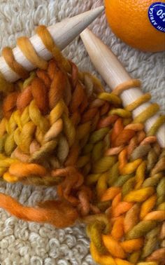 an orange sits next to several different colored yarns on a white rug with two skewers