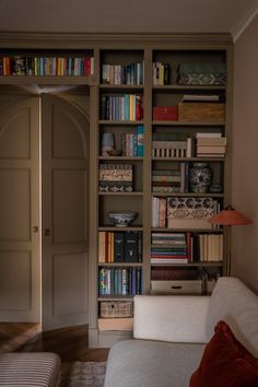 a living room filled with lots of books on top of a book shelf next to a white couch