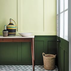 a room with green walls and a wooden table in the corner, next to a basket