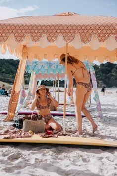 two women in bikinis under an umbrella on the beach