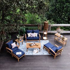 an outdoor patio with blue cushions and wooden furniture on the deck, surrounded by greenery