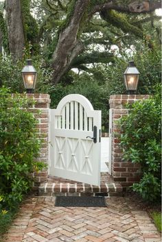 an image of a white gate in the middle of a brick walkway with two lights on each side