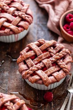 raspberry pies on a wooden table with spoons and fork next to them