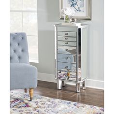 a mirrored jewelry cabinet with drawers in front of a blue chair and white flower arrangement