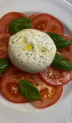 a white plate topped with sliced tomatoes and an egg on top of basil leafy greens