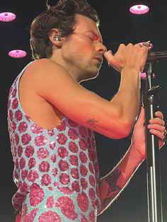 a man in a pink and blue dress holding a microphone to his mouth while standing on stage