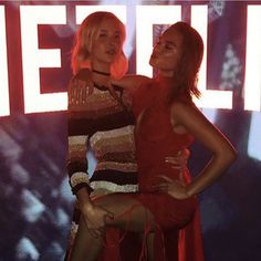 two beautiful women standing next to each other in front of a neon sign with the word hello written on it