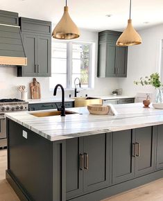 a large kitchen with gray cabinets and white counter tops, gold pendant lights over the island