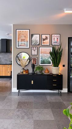 a living room with pictures on the wall and plants in vases next to it