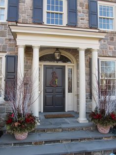 two planters with red flowers are on the front steps of a large brick house