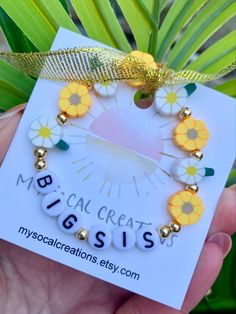 a hand holding a yellow and white bracelet with daisies on it, that says medical creations