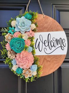 a welcome sign hanging on a door with flowers and greenery in front of it