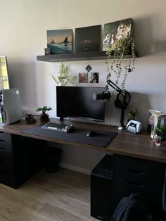 a desk with a computer monitor, keyboard and mouse on it next to a plant