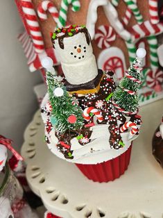 a cupcake decorated like a snowman with candy canes on the side and christmas decorations around it