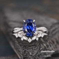 a blue sapphire and diamond ring set on top of a piece of wood with leaves around it