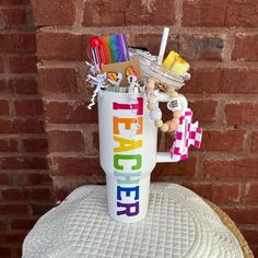 a cup that is sitting on top of a table with toys in it and the words teacher spelled out