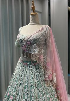 a green and pink lehenga on display in front of a curtained window