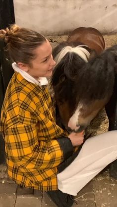 a woman kneeling down next to a brown and white horse