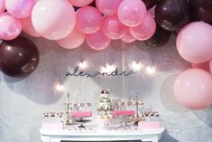 a table topped with lots of pink and brown balloons next to a wall covered in balloons