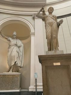 two statues in the middle of a room with white walls and arches on either side