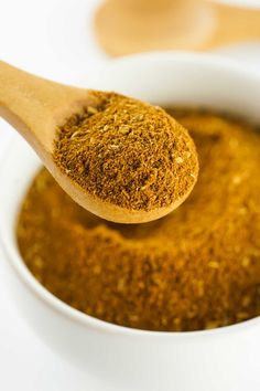 a wooden spoon full of spices in a white bowl