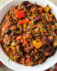 a white bowl filled with chili and beans on top of a wooden table next to a napkin