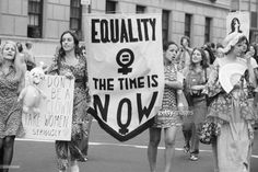 some women are marching down the street holding signs that read equality and the time is now