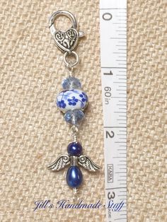 a blue and white beaded charm with angel charms on it next to a measuring ruler